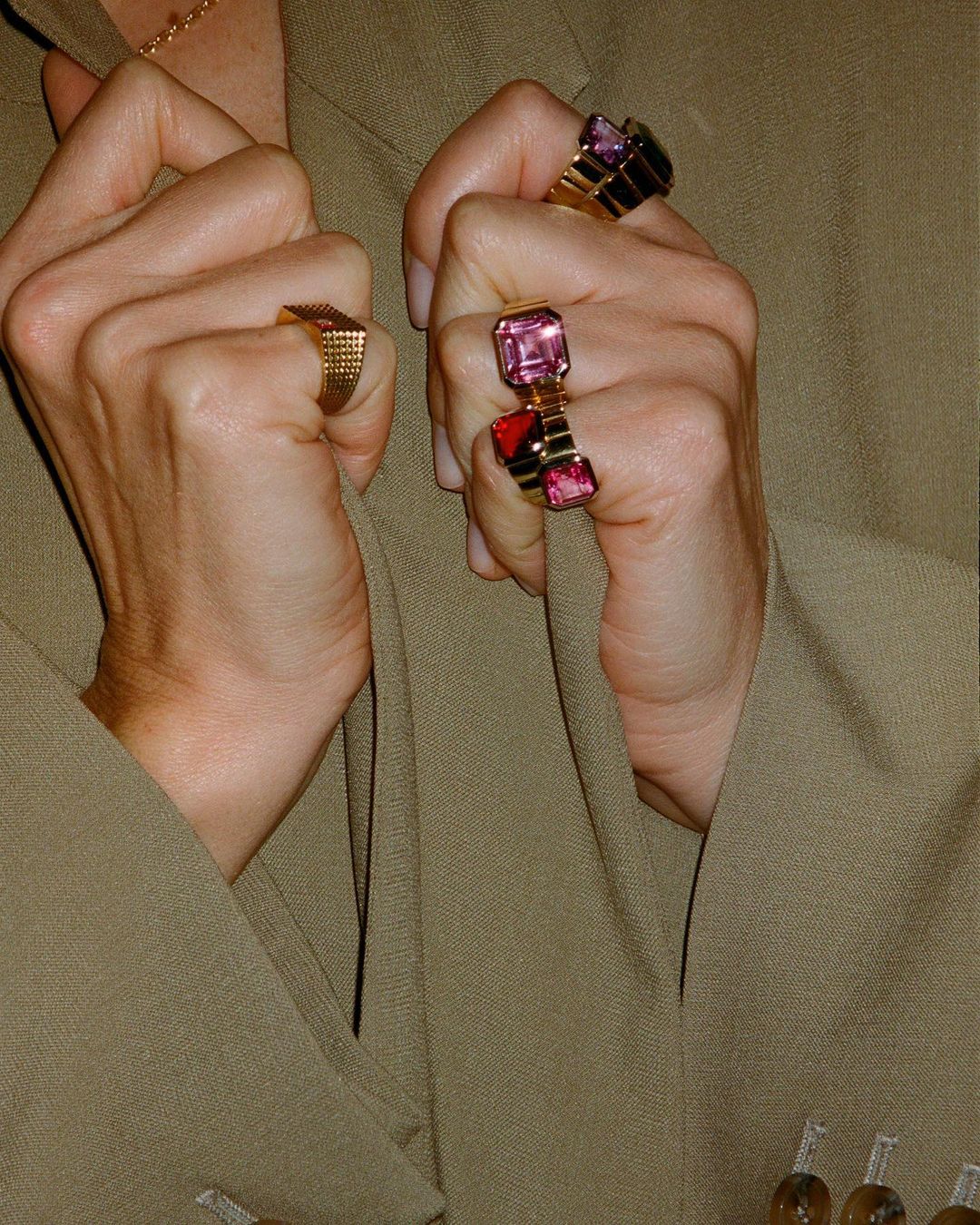 Close-up of fair-skinned woman's hands adorned with statement rings against a beige jacket, highlighting fashion jewelry and textures.