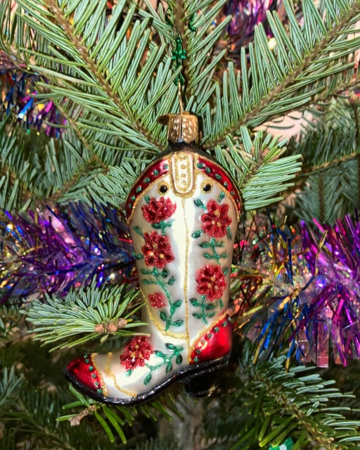 Christmas tree decorated with a cowboy boot ornament featuring red flowers, gold trim, and a glossy finish, creating a festive holiday scene.