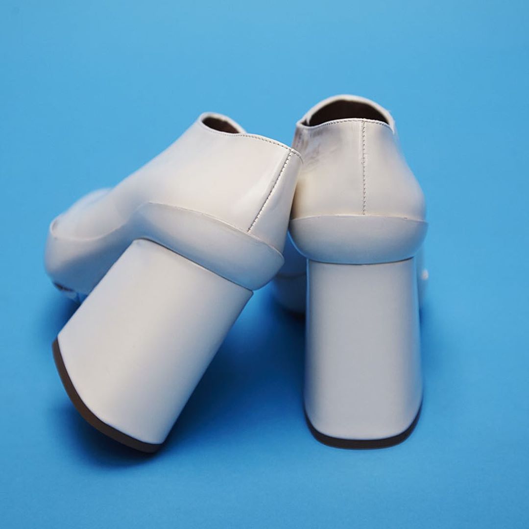 White platform heeled shoes are displayed against a bright blue backdrop in this studio shot, showcasing their modern design.