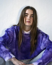 Portrait of a woman wearing a purple knit sweater against a plain white textured background photographed by Thierry Lebraly