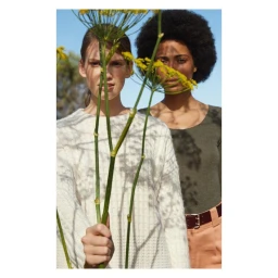 Two female models posing behind tall yellow wildflowers against a clear blue sky, photographed by Thierry Lebraly.