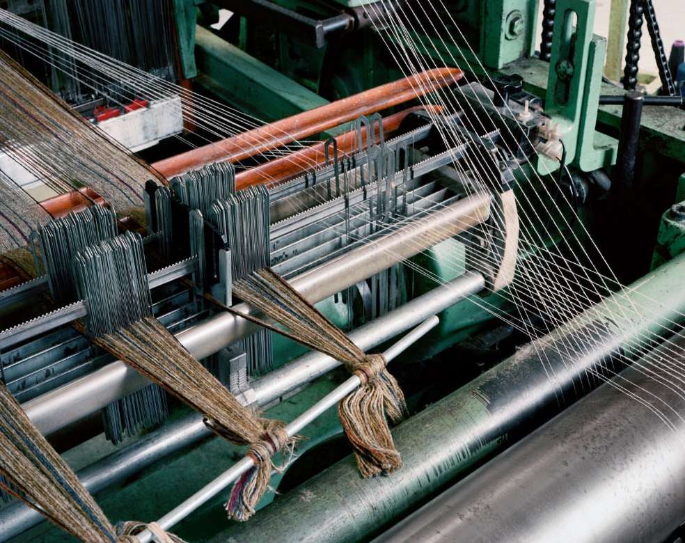 Close-up of a weaving machine with visible threads and metallic components in industrial setting, highlighting textile production.