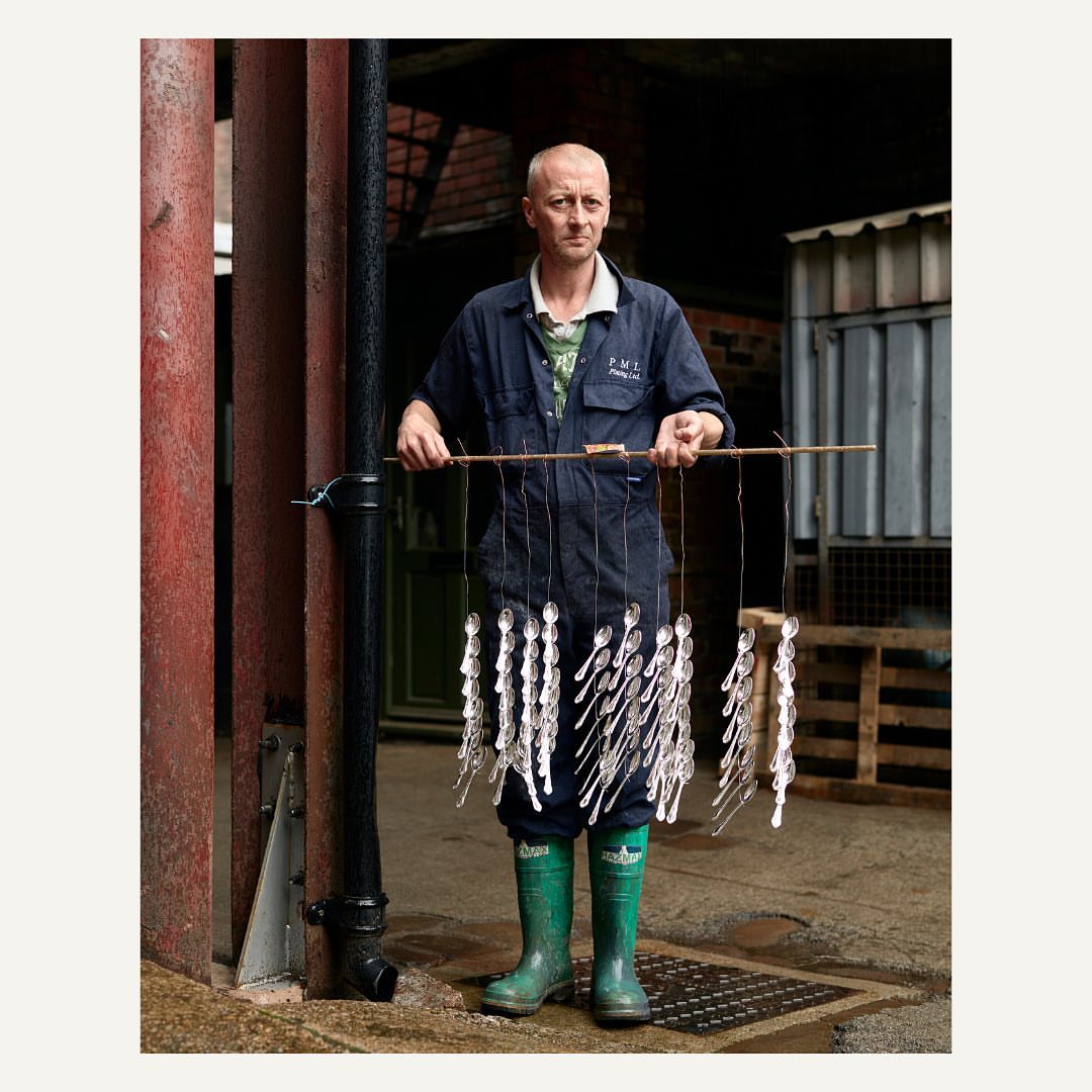 A man in work clothes holds a rack of spoons outdoors in an industrial setting, showcasing everyday life and craftsmanship.