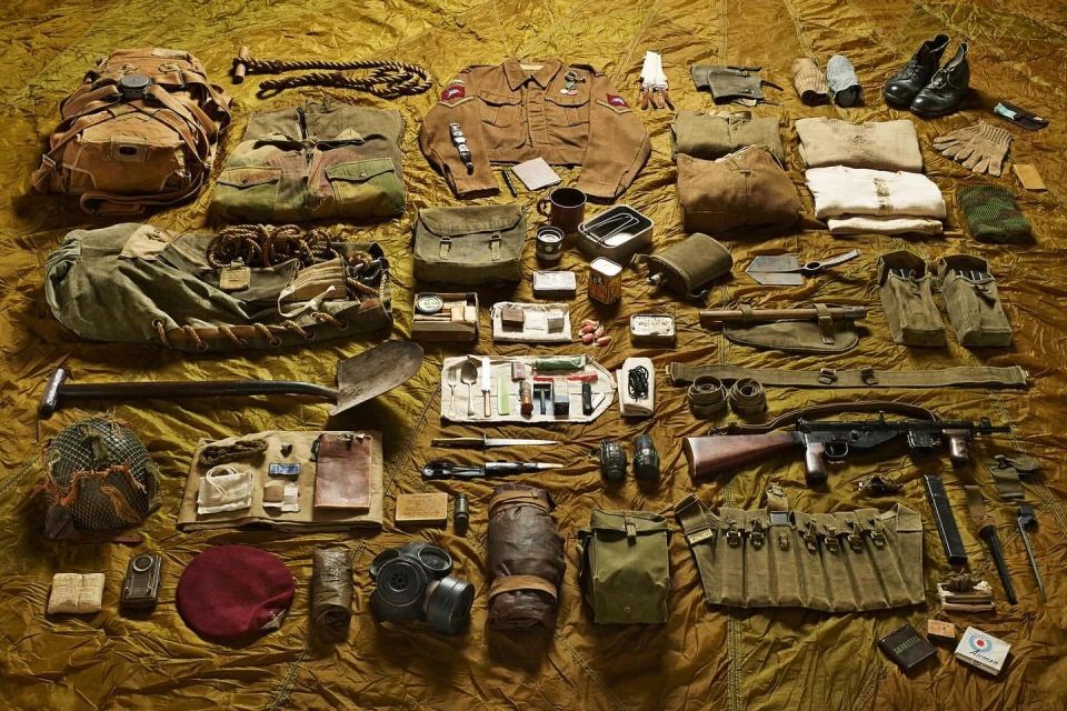 Overhead shot of vintage military equipment and clothing laid out on a textured brown cloth, creating a detailed archival display.