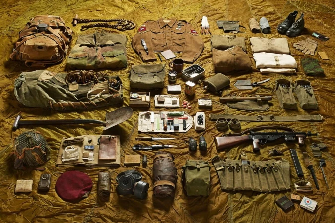 Overhead shot of vintage military equipment and clothing laid out on a textured brown cloth, creating a detailed archival display.