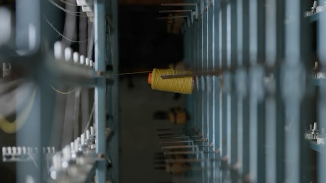 Close-up of a textile machine with a vibrant yellow thread spool, showcasing the industrial manufacturing process in a factory setting.