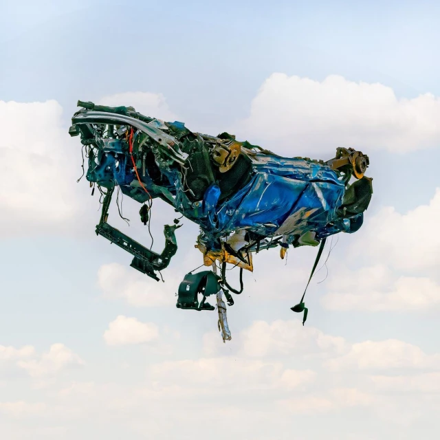 Conceptual image of a crushed and twisted blue car body suspended against a backdrop of a blue sky with scattered clouds.