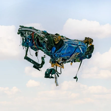 Conceptual image of a crushed and twisted blue car body suspended against a backdrop of a blue sky with scattered clouds.