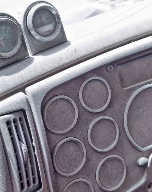 Close-up of a vehicle dashboard with gauges and air vents, featuring a textured, neutral-toned surface and circular design elements.