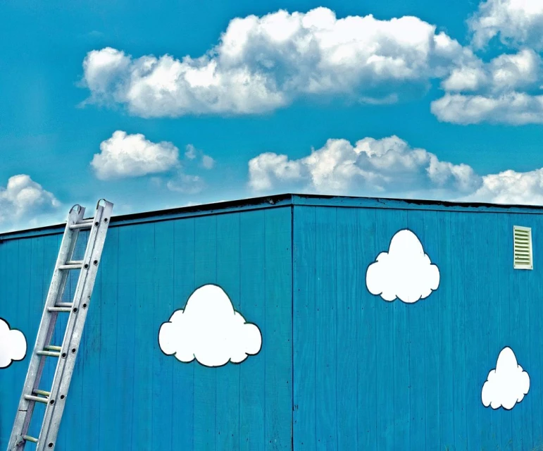 A blue building with white clouds painted on the side and a silver ladder leaning against the building under a blue sky with clouds.