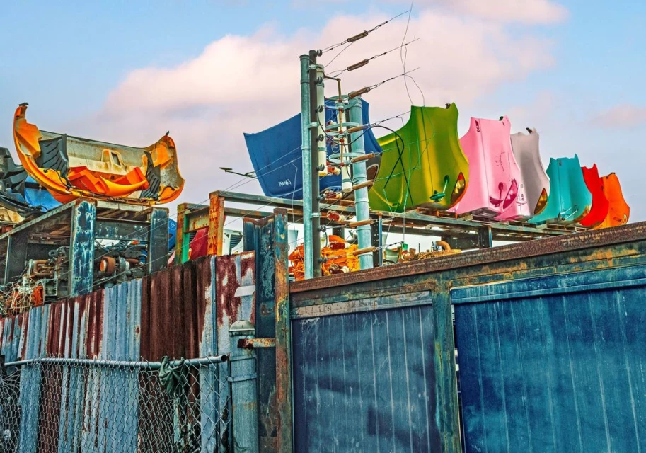 Colorful array of car hoods displayed on a rusted metal structure under a bright sky, creating an automotive scrapyard scene.