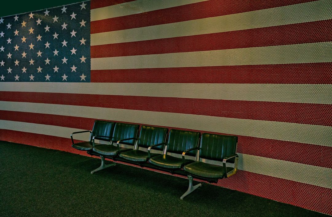 Row of empty green chairs in front of a wall displaying the American flag created from colored tiles.