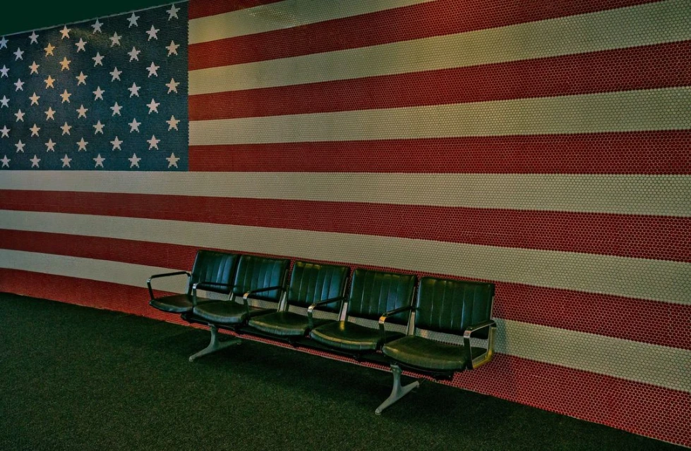 Row of empty green chairs in front of a wall displaying the American flag created from colored tiles.