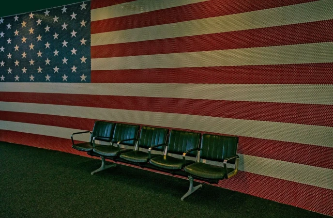 Row of empty green chairs in front of a wall displaying the American flag created from colored tiles.
