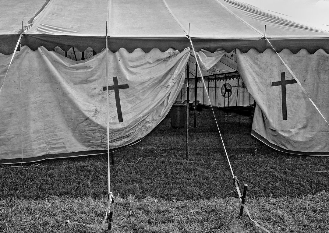 Black and white shot of a white tent with cross designs, set on grassy ground, evoking a vintage or documentary feel.