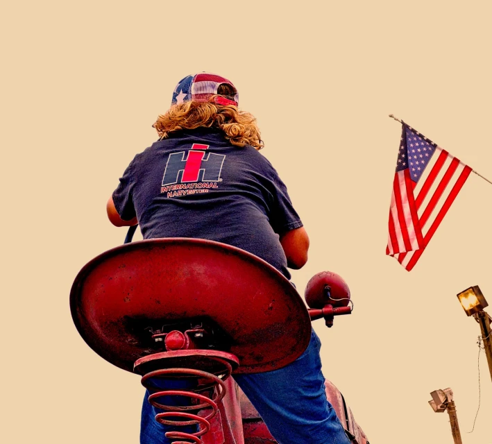 Person on a red tractor-shaped spring rider, wearing a USA flag hat and a navy blue shirt with the International Harvester logo.