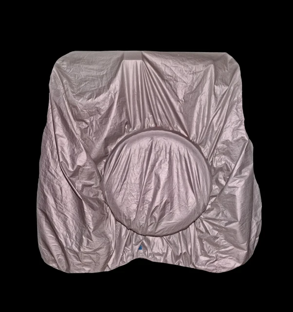 Silver car with a cover on top in a studio with black background, the cover is draped over the entire vehicle, obscuring its features.