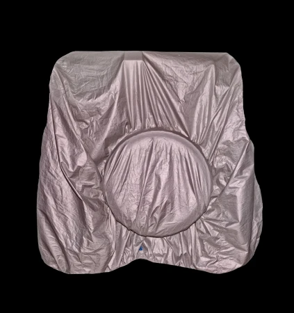 Silver car with a cover on top in a studio with black background, the cover is draped over the entire vehicle, obscuring its features.