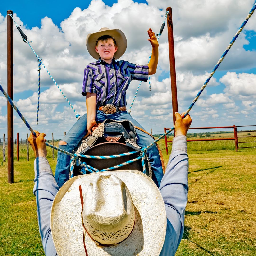 A young boy in a cowboy hat and striped shirt on a horse-like swing, photographed by Thom Gilbert in New York.