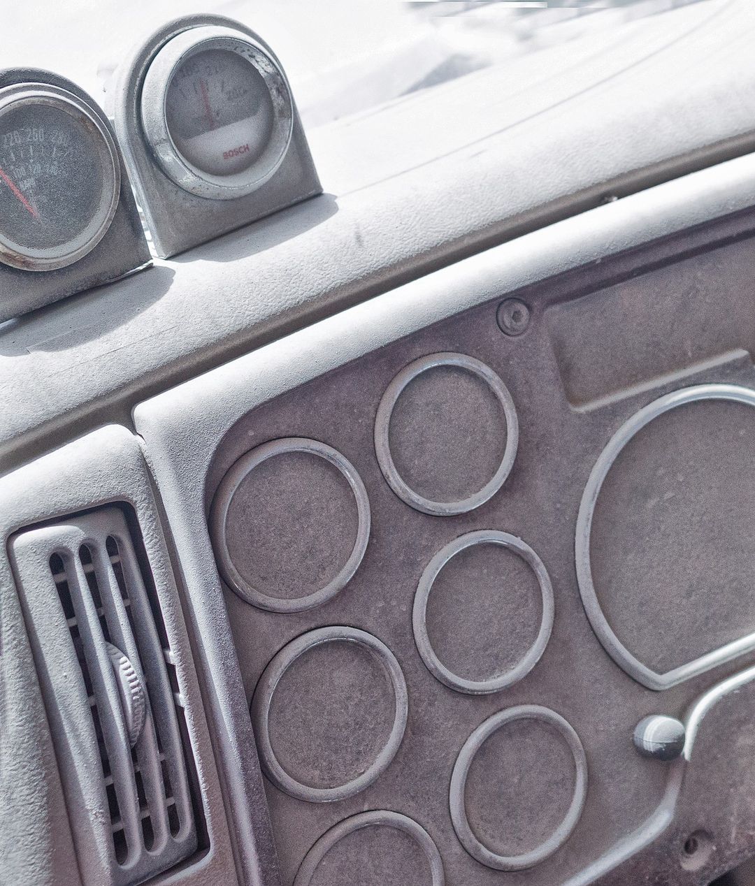 Close-up of an automotive dashboard with gauges, air vent, and circular switch plates in muted grayscale, providing an industrial feel.