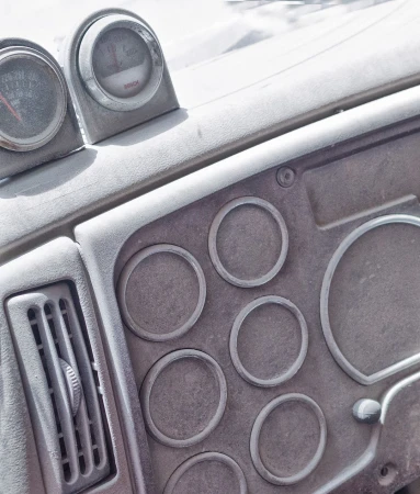 Close-up of an automotive dashboard with gauges, air vent, and circular switch plates in muted grayscale, providing an industrial feel.