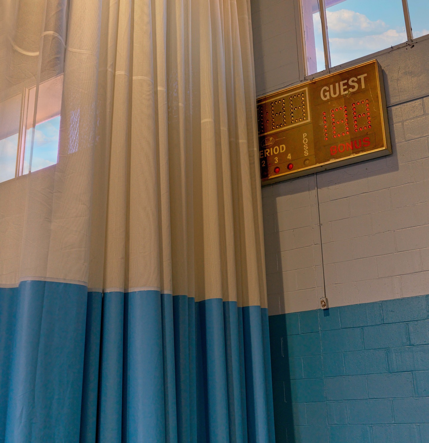 Indoor view of a blue and white curtain, a scoreboard displaying the word 'Guest', and natural light from a window illuminating the scene.