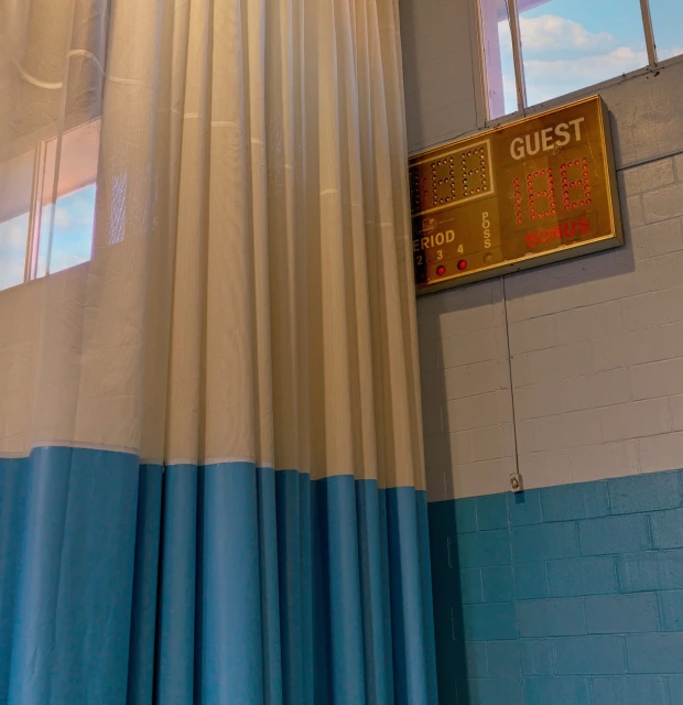 Indoor view of a blue and white curtain, a scoreboard displaying the word 'Guest', and natural light from a window illuminating the scene.