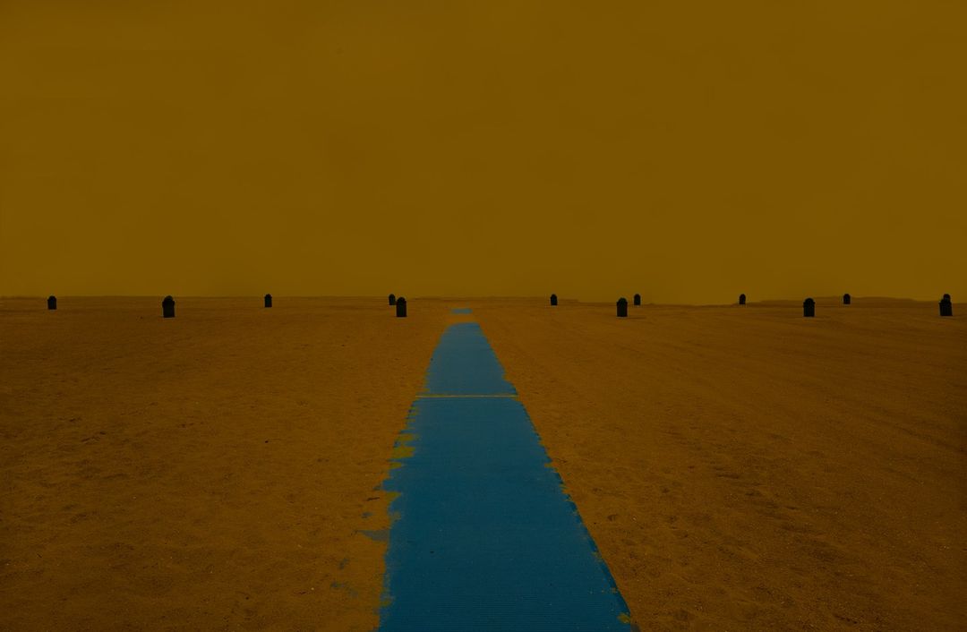 Abstract landscape with blue river flowing through sandy terrain under a gold sky, featuring sparse dark monoliths.