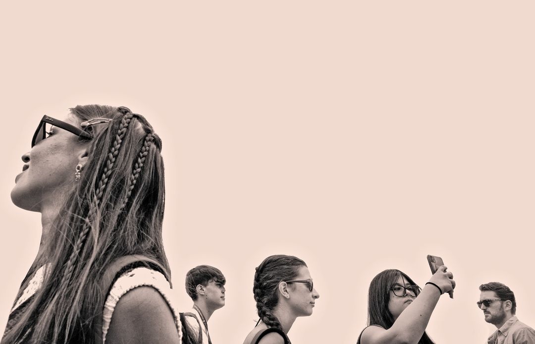 Silhouetted group of young adults outdoors in monochrome, wearing sunglasses and modern clothing, looking up at a high angle.