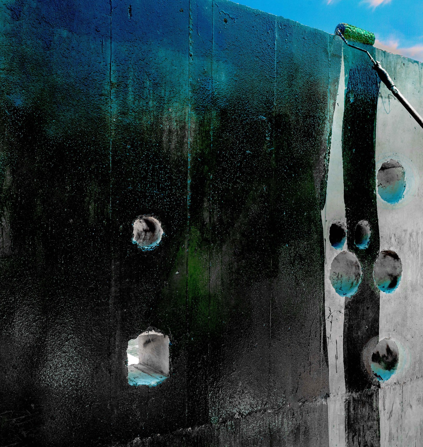 Roller applies paint to a concrete wall with square and round holes against a bright blue sky with sparse clouds, high contrast.