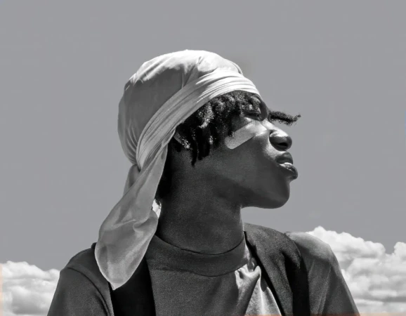 Black man wearing a silky durag and t-shirt against a cloudy sky background in New York by photographer Thom Gilbert.