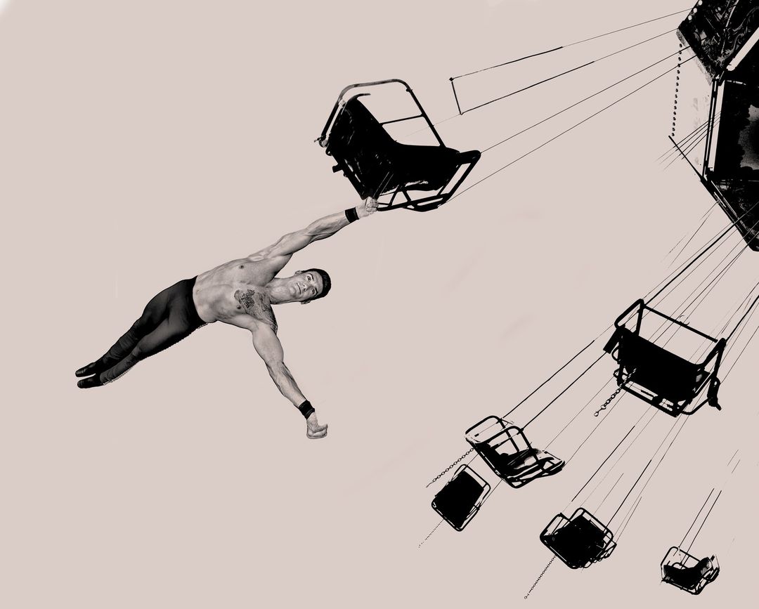 An artistic monochrome image shows a shirtless male gymnast holding onto a carousel swing with other swings visible in the background.