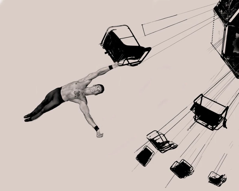 An artistic monochrome image shows a shirtless male gymnast holding onto a carousel swing with other swings visible in the background.