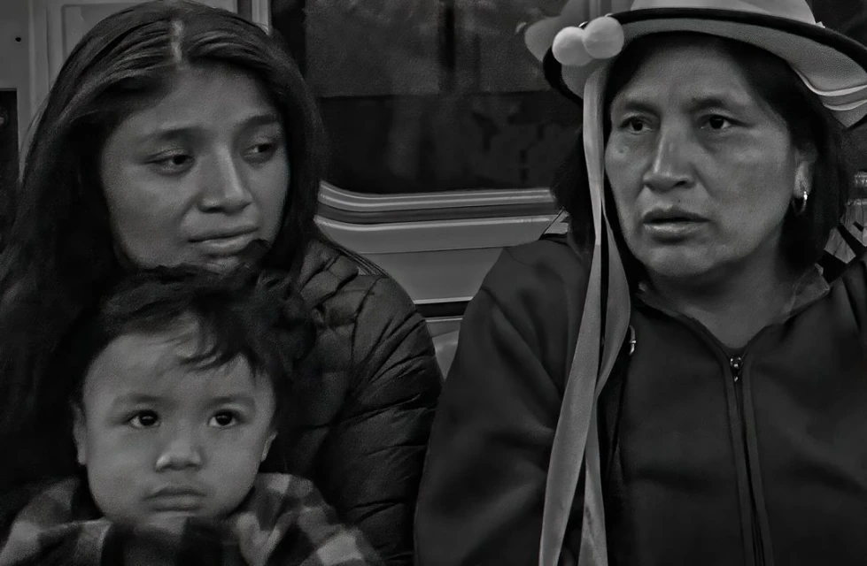 Black and white photo of three people sitting indoors. The group features a child in the foreground and two women behind.