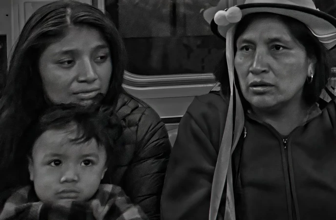 Black and white photo of three people sitting indoors. The group features a child in the foreground and two women behind.