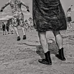 Monochrome beach scene with people jumping and walking on sand captured by photographer Thom Gilbert in New York