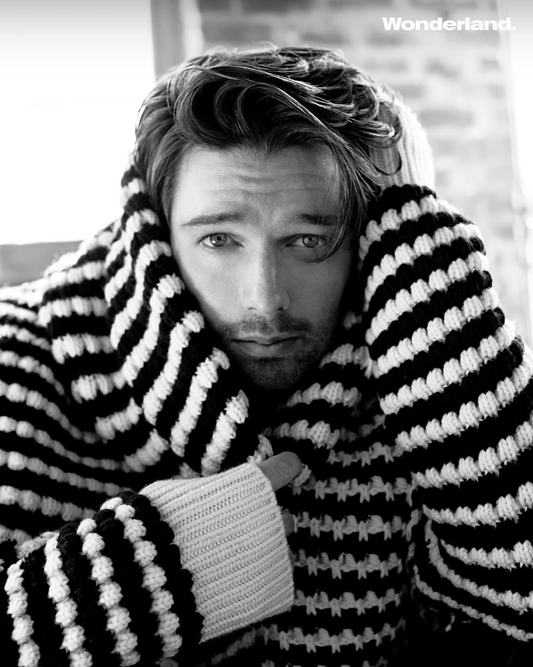 Black and white portrait of a man wearing a chunky knit sweater. He is looking directly at the camera with a serious expression.