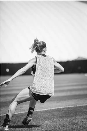 Monochrome image of a woman in athletic wear running on a grassy field with a large, white dome in the background on a sunny day.