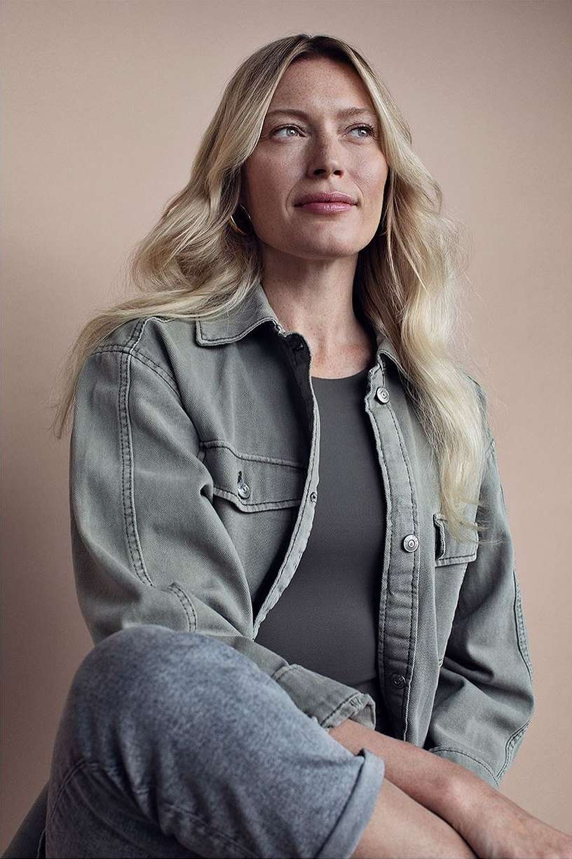 Portrait of a blonde woman wearing an olive green jacket against a neutral studio background