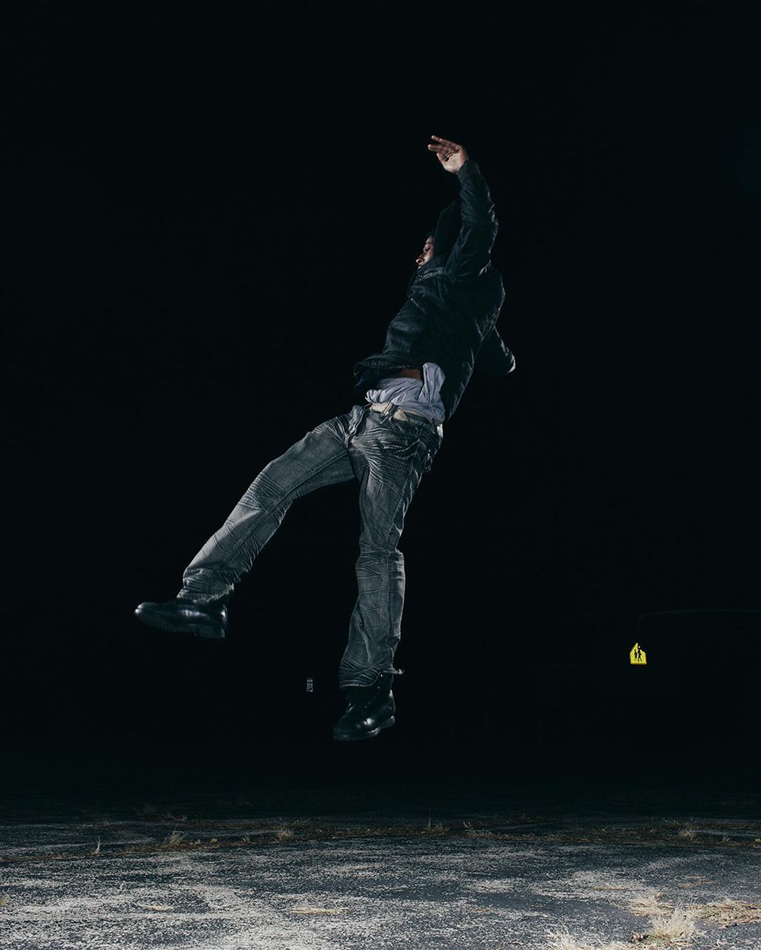 A man is captured mid-air in a jump, wearing jeans and a jacket against a dark backdrop, suggesting a dynamic outdoor shot with focus on movement.