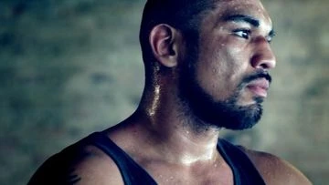 Close-up of a sweaty adult male athlete in a tank top, focused expression, in a workout environment. Fitness and determination.