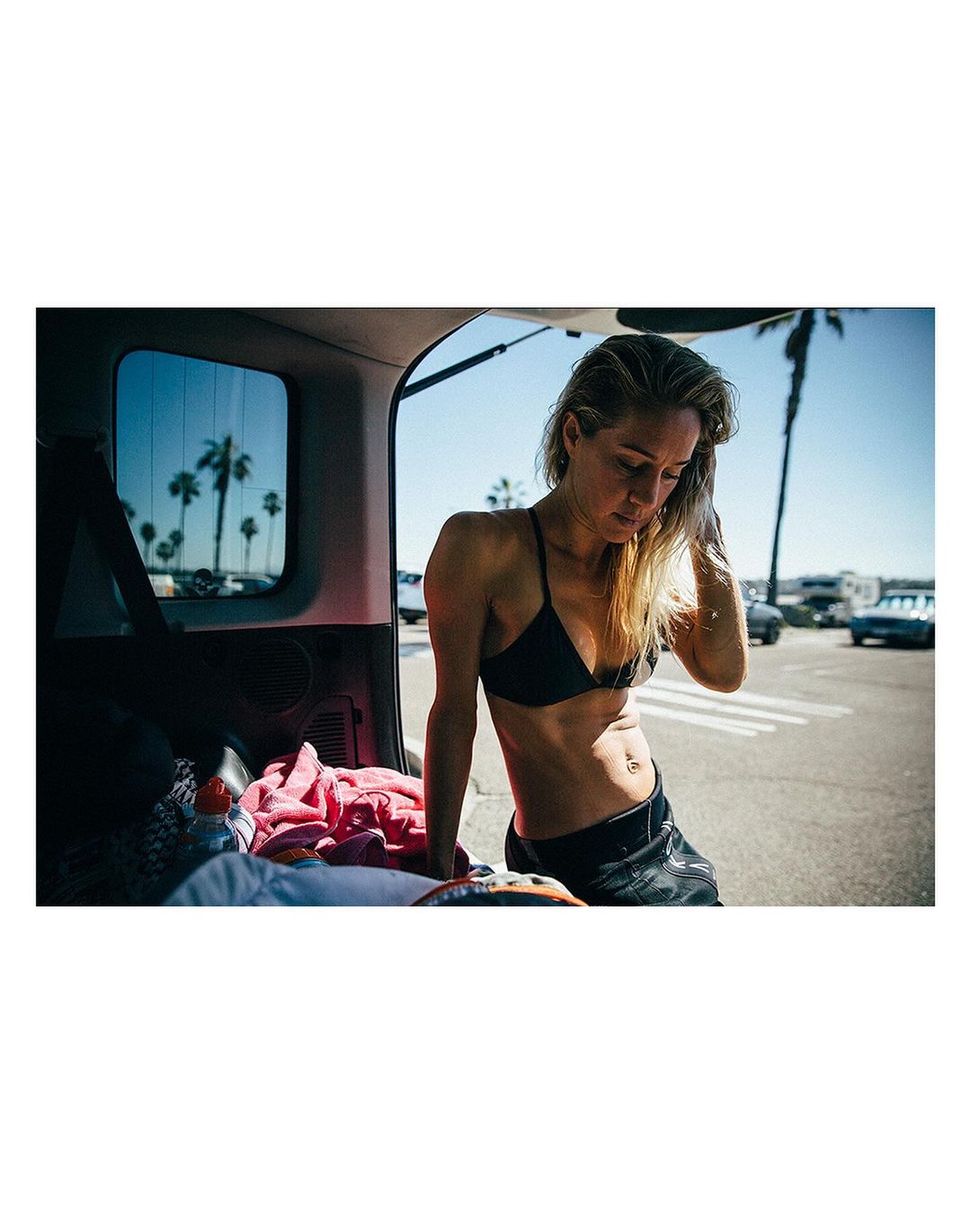 Woman in bikini top leaning out of a vehicle trunk in a sunny parking lot