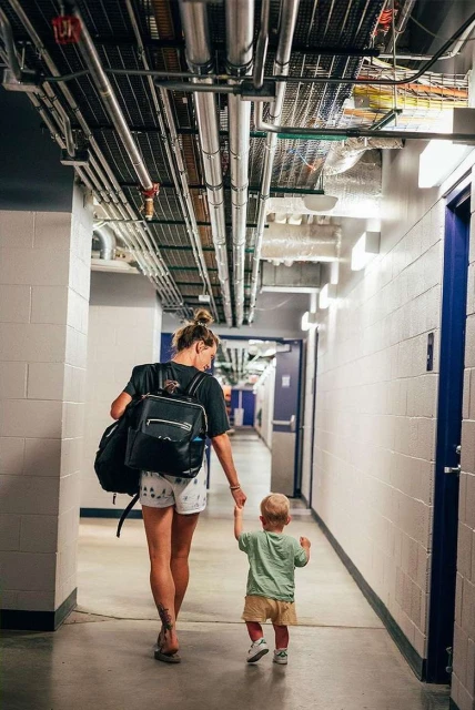 Woman and toddler walking away down an indoor hallway, woman carries a backpack and the child holds her hand.