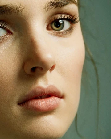 Close-up portrait of a fair-skinned woman with hazel eyes, focusing on her facial features against a muted teal background.