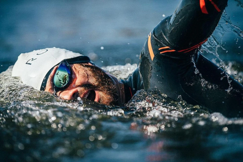 Adult male swimmer in wetsuit, swimming goggles, and swim cap in open water, capturing the essence of a triathlon competition.