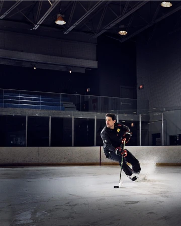 Ice hockey player in action on an ice rink, gliding with a hockey stick and puck, wearing full protective gear and uniform.