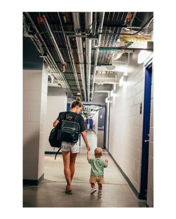 A woman and toddler walk away from the camera down a corridor lined with doors and exposed utility pipes.