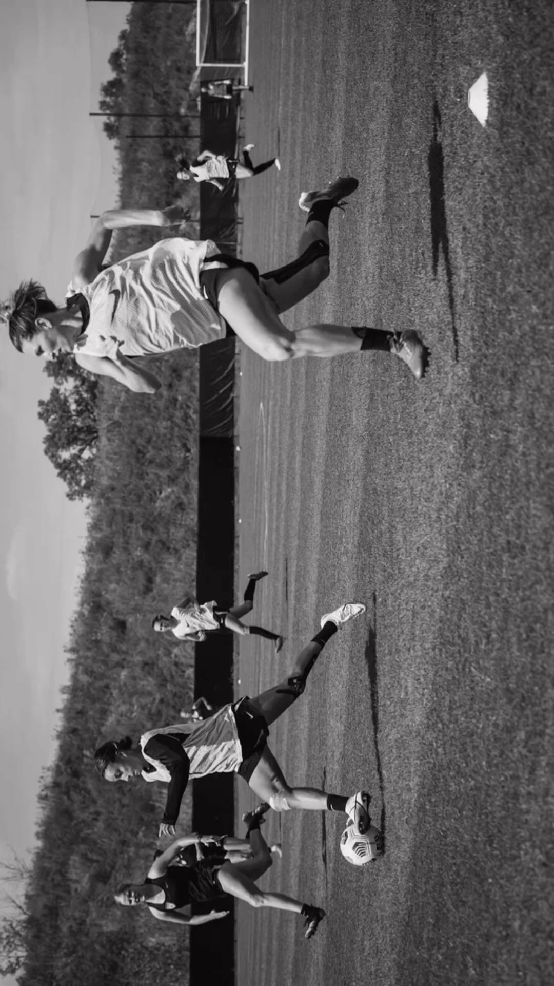 Several female athletes compete in a black and white soccer match on a grassy field during daylight. The field extends to the horizon.