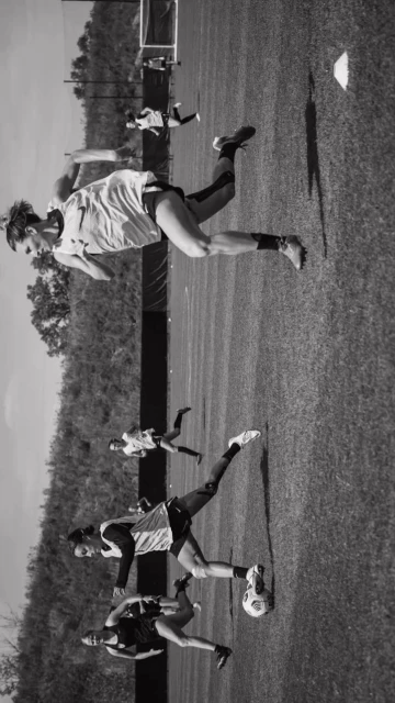 Several female athletes compete in a black and white soccer match on a grassy field during daylight. The field extends to the horizon.