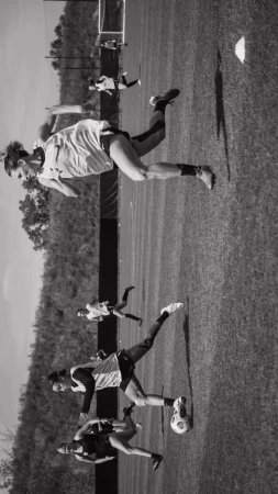 Several female athletes compete in a black and white soccer match on a grassy field during daylight. The field extends to the horizon.